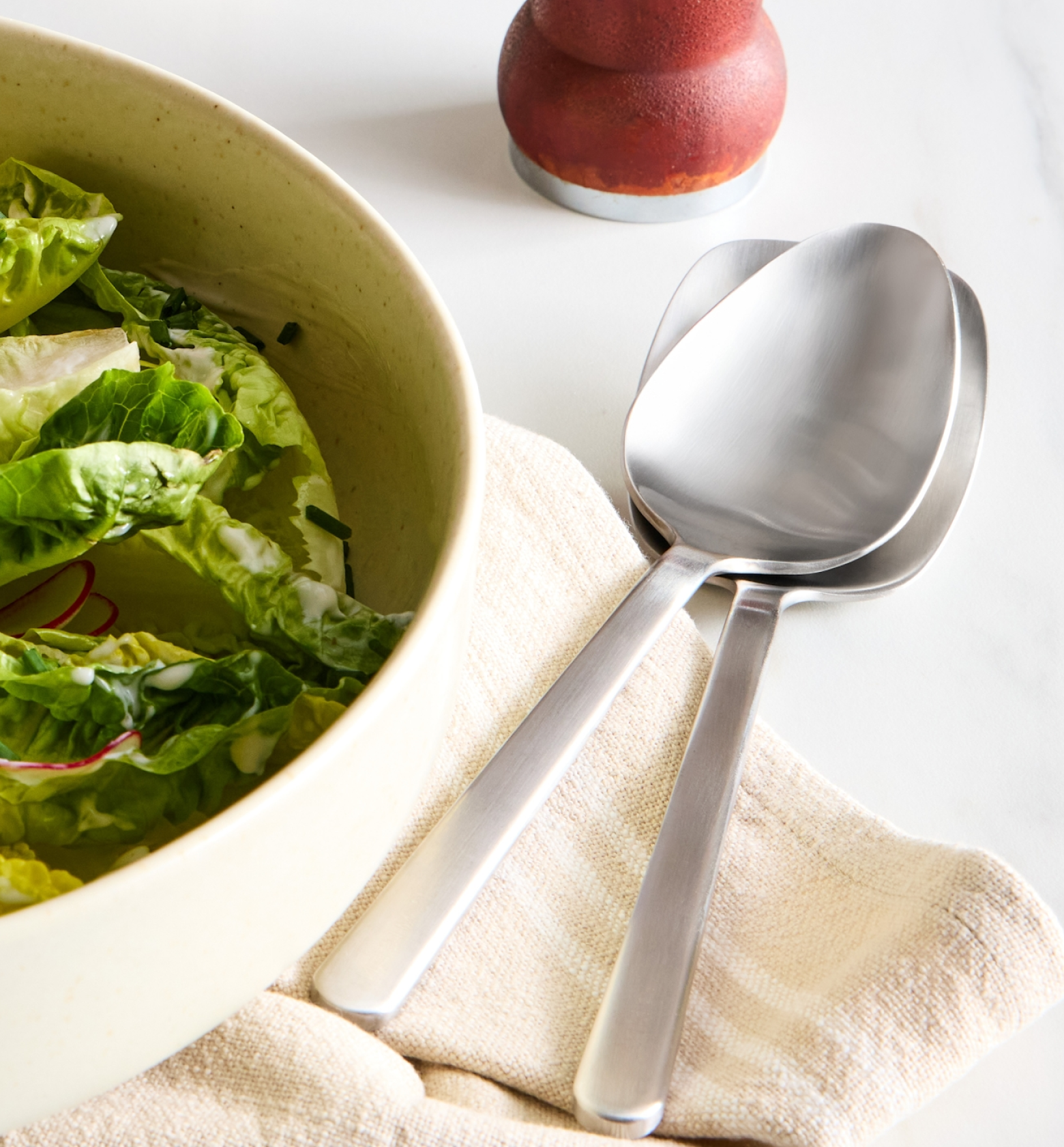 Stainless steel salad serving spoons beside a bowl of romaine lettuce salad